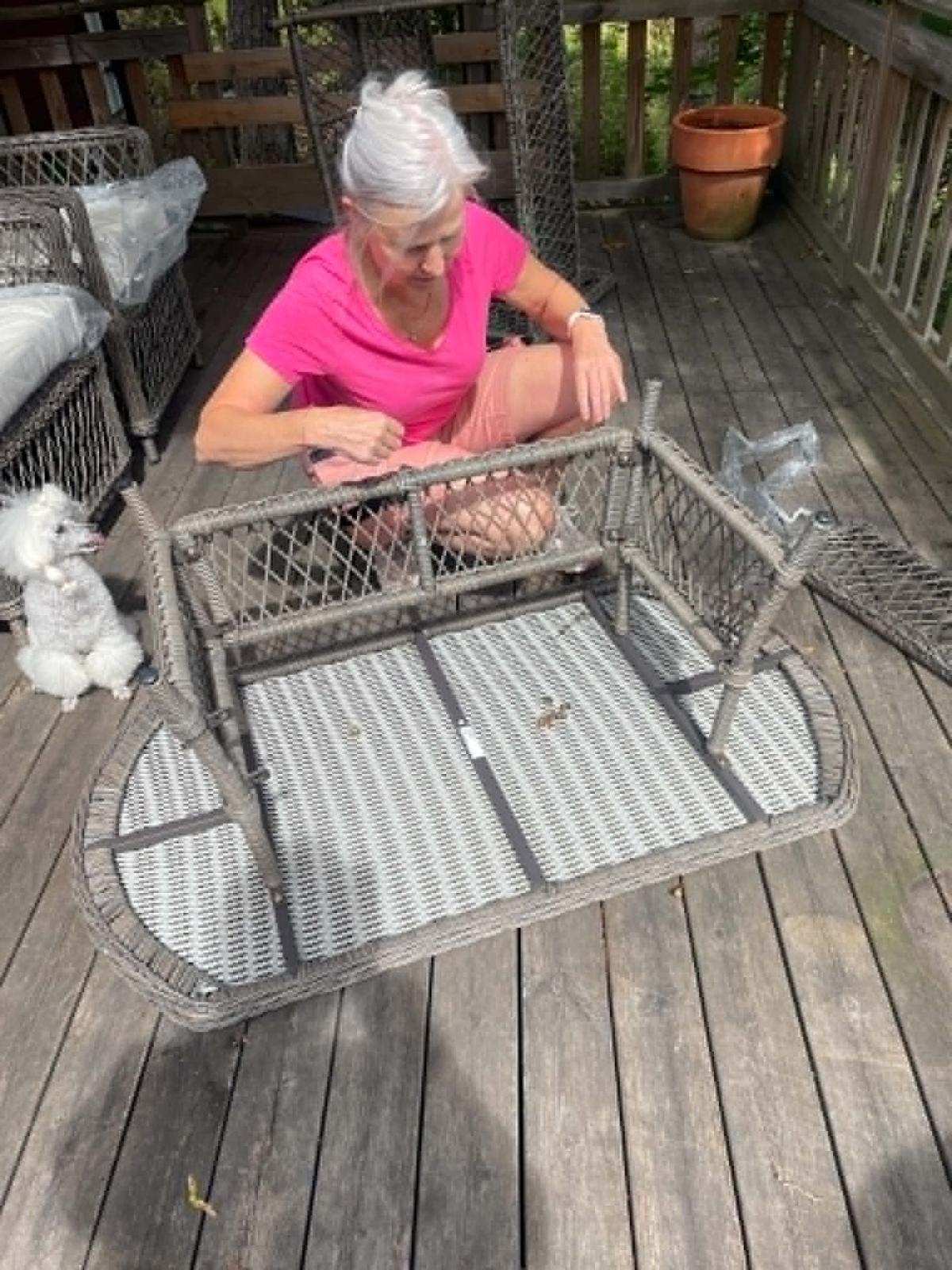 Annica monterar ett trädgårdsbord på en terrass, pudeln Olle sitter bredvid